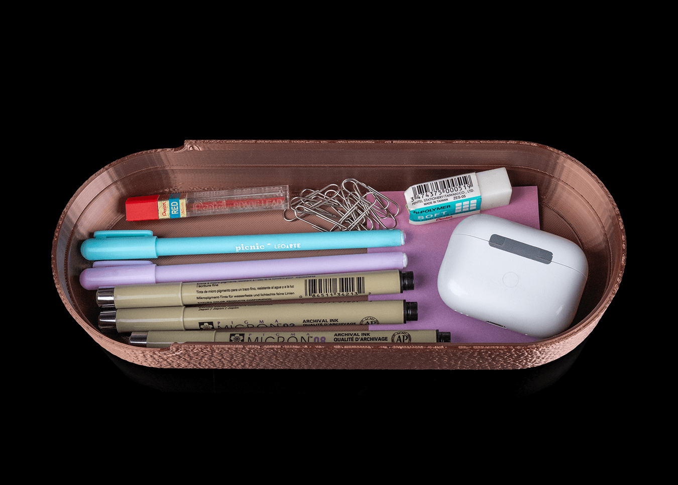 Small container with stationery items including pens, markers, and a white object on a black background