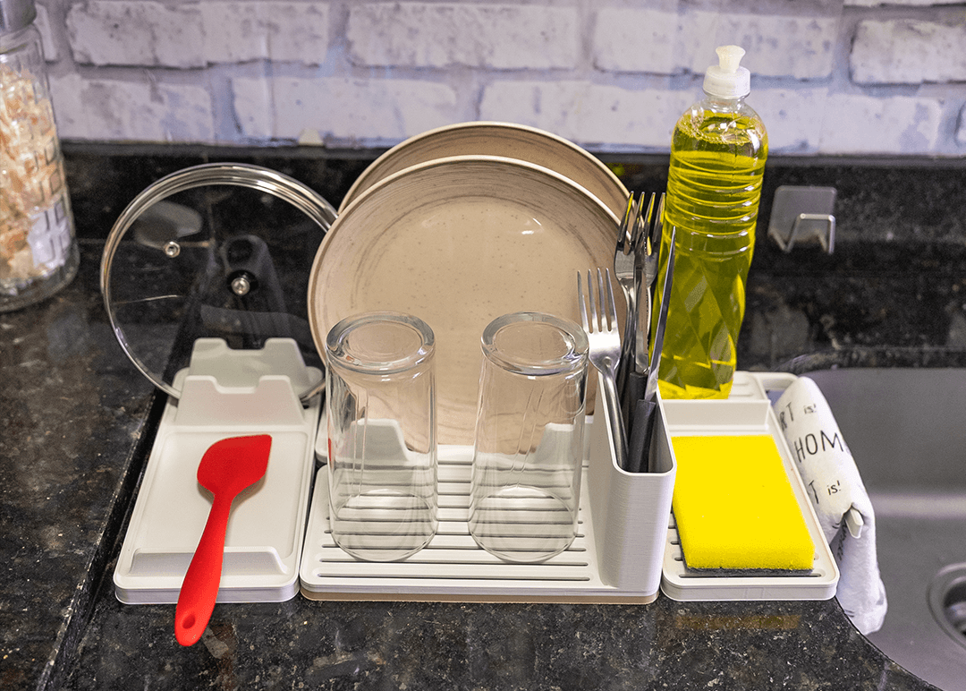 Dish drying rack with plates, glasses, and utensils on a kitchen counter.